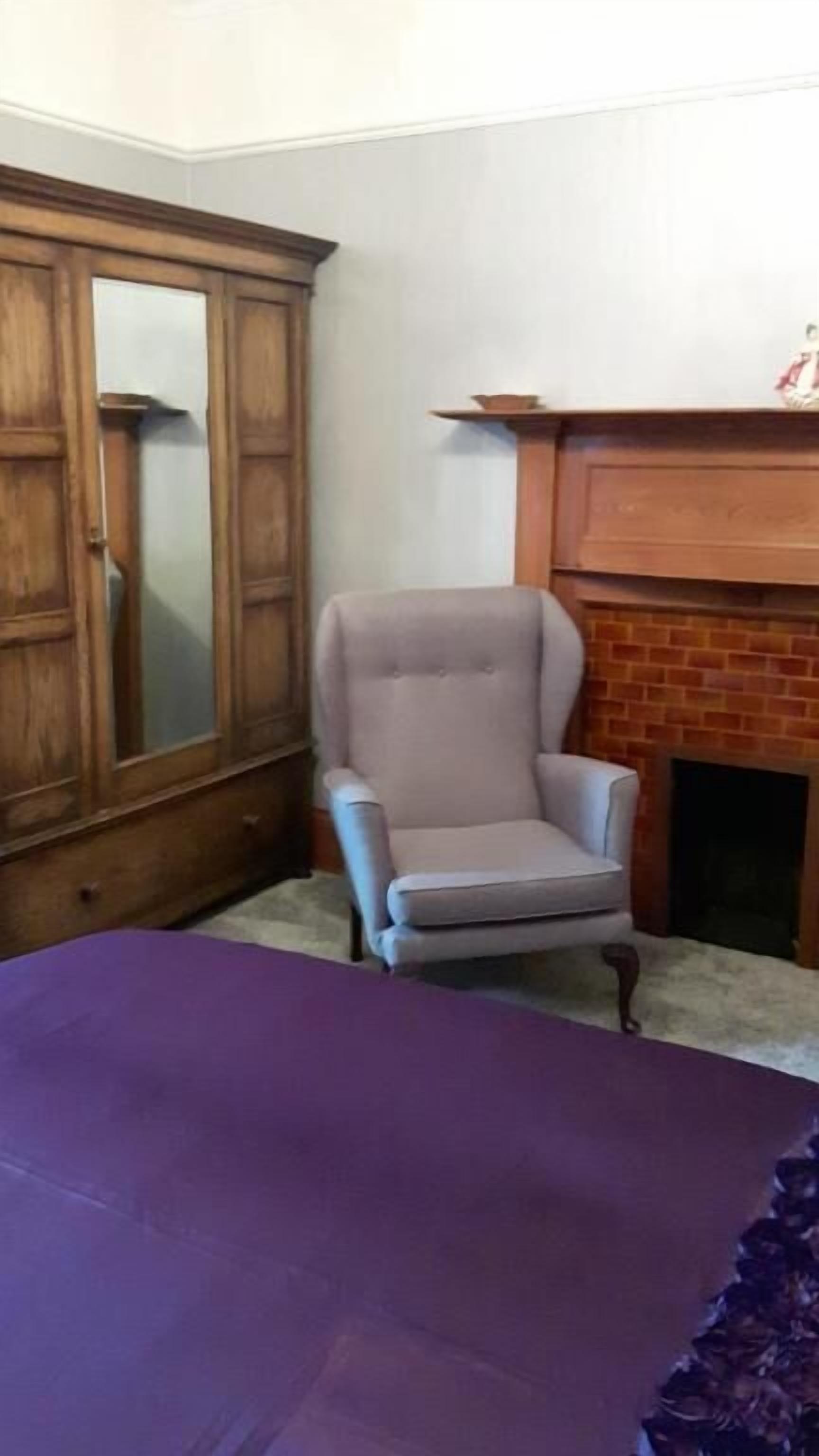 A room with a wooden wardrobe, a grey armchair, and a fireplace.