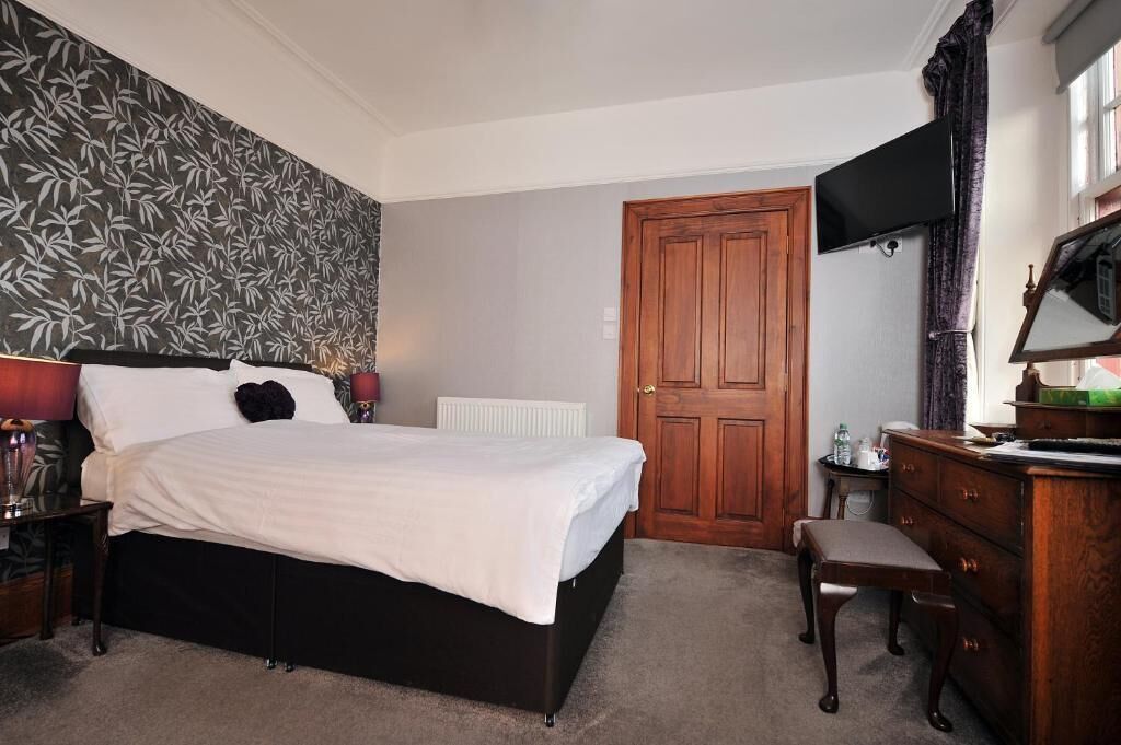 A hotel room with a large bed, a wooden dresser, a desk, a television, and a door.