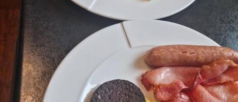Two plates of breakfast food including sausages, bacon, mushrooms, and scrambled eggs.