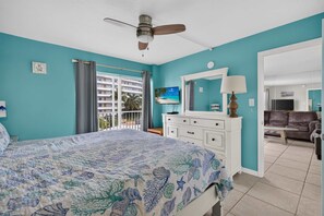 A bedroom with a bed, a ceiling fan, a TV, and a view of a building outside. - Beach   Pool Open  Beachfront View Every Room (Siesta Key)