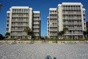A beachfront hotel with multiple floors, balconies, and a sandy beach area with sun loungers. - Beach   Pool Open  Beachfront View Every Room (Siesta Key)