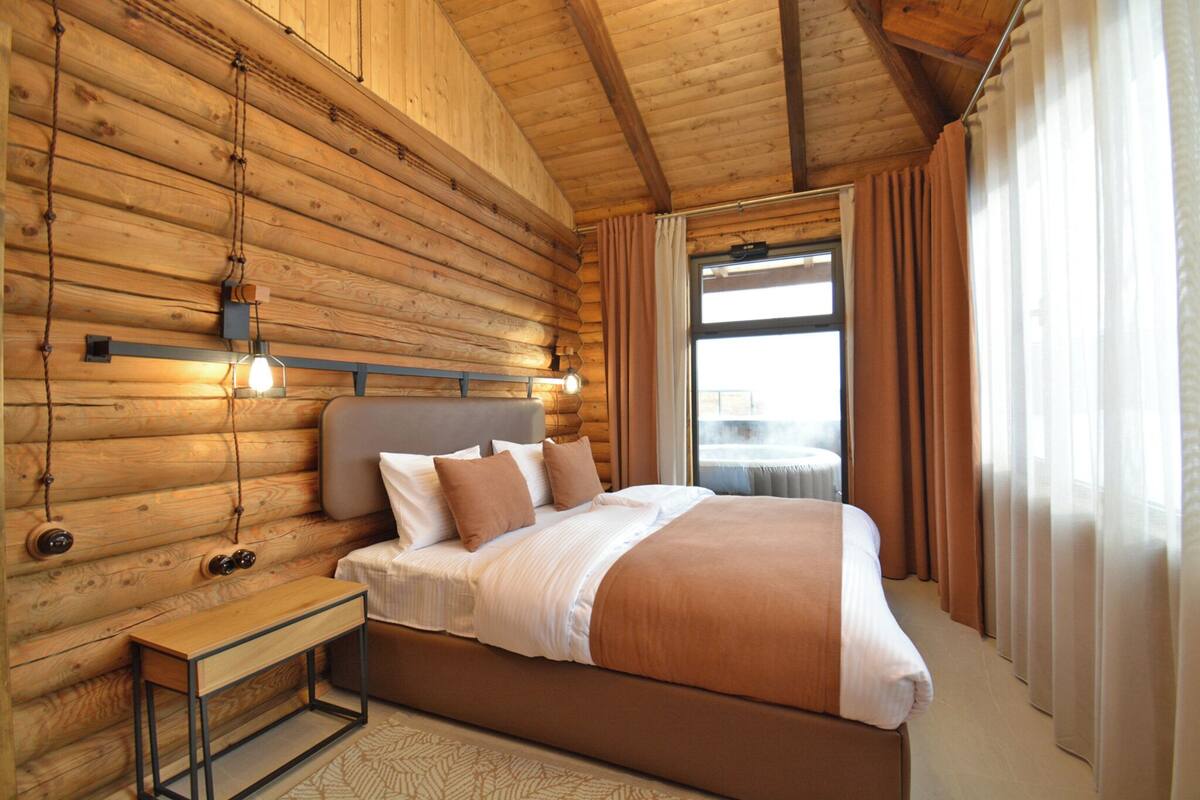 A log cabin-style bedroom with a bed, bedside table, and hanging light fixtures.