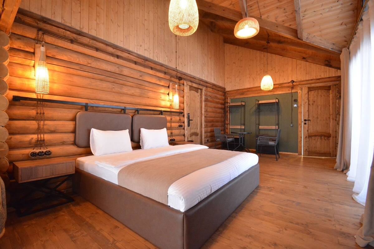 A log cabin-style bedroom with a large bed, wooden walls, and hanging light fixtures.