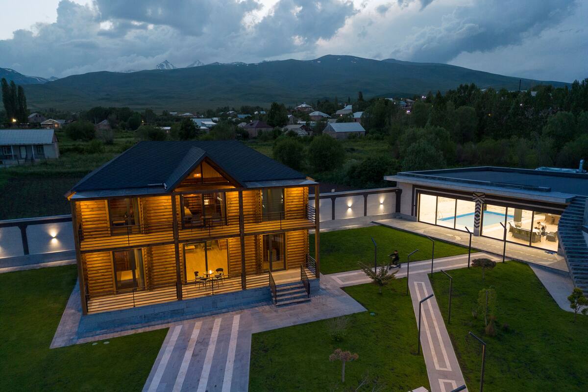 A modern two-story house with a large glass facade, a visible pool, and a well-maintained lawn.