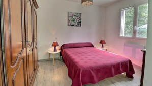 Une chambre à coucher avec un lit, deux tables de chevet avec des lampes, une armoire en bois, un tableau au mur et une fenêtre donnant sur un paysage verdoyant.