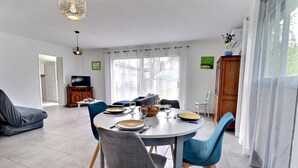 Un coin repas avec une table ronde, des chaises bleues et un téléviseur en arrière-plan.