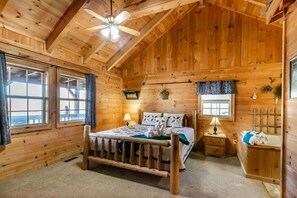 Ein Schlafzimmer einer Holzhütte mit Bett, Nachttischen, einem Fenster und einem Deckenventilator.