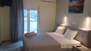 Una habitación de hotel con cama, mesita de noche, ventana con cortinas y un cuadro en la pared.