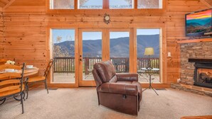 A cozy log cabin interior with a dining area, leather chair, fireplace, and large windows overlooking mountains. - Gorgeous View Cabin  Hot Tub  Privacy  Fireplace  Pool   Fishing Access (Sevierville)