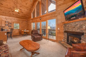 Ein geräumiges Holzhütten-Interieur mit Essbereich, Kamin und Wand-Fernseher.