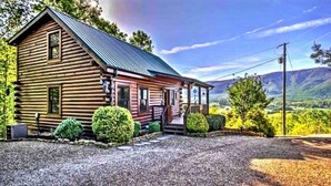 A log cabin with a porch, surrounded by greenery and a mountainous backdrop. - Gorgeous View Cabin  Hot Tub  Privacy  Fireplace  Pool   Fishing Access (Sevierville)