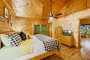 A wooden cabin bedroom with a bed, dresser, television, and ceiling fan. - Location  Log Cabin Hot Tub Fireplace Pool Fishing (Pigeon Forge)