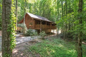 A rustic log cabin with a porch, surrounded by dense forest. - Location  Log Cabin Hot Tub Fireplace Pool Fishing (Pigeon Forge)