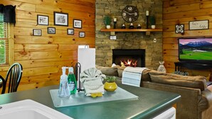 L’intérieur d’un chalet accueillant, avec des murs en bois, une cheminée en pierre, une horloge, des tableaux encadrés et un téléviseur.