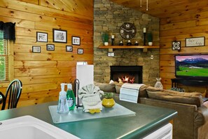 L’intérieur d’un chalet accueillant, avec des murs en bois, une cheminée en pierre, une horloge, des tableaux encadrés et un téléviseur.