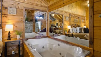Interior de una cabaña de madera con un espejo grande, una bañera y un dormitorio acogedor con cama y almohadas.