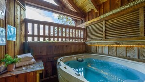 A wooden spa area with a hot tub, wooden benches, and a view of the outdoors. - Location  Cute Studio Log Cabin Hot Tub Fireplace (Pigeon Forge)