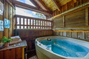 Een houten wellnessruimte met een jacuzzi, houten banken en uitzicht op de natuur.