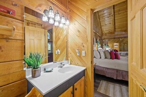 A wooden cabin interior with a bathroom featuring a white sink, a mirror, and a potted plant. - Location  Cute Studio Log Cabin Hot Tub Fireplace (Pigeon Forge)