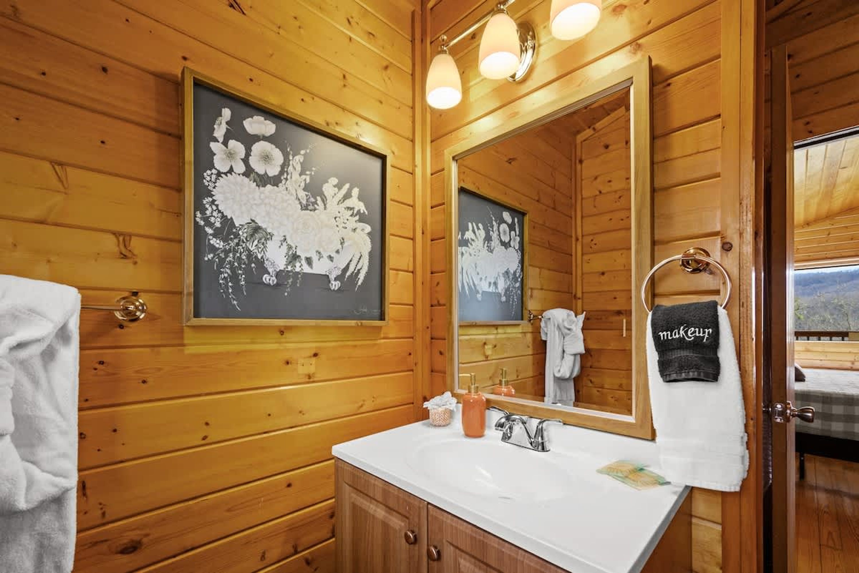 Une salle de bain rustique, avec des murs en bois, un grand miroir, un lavabo et un porte-serviettes.