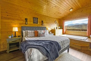 A cozy wooden cabin bedroom with a large bed, a nightstand with a lamp, a window with a view of mountains, and a motivational quote on the wall. - Great View  Location  Studio Log Cabin  Hot Tub (Gatlinburg)