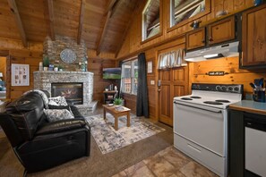 Ein gemütliches Blockhaus-Interieur mit Kamin, einer Küche mit Herd, einem Ledersofa und Holzwänden.