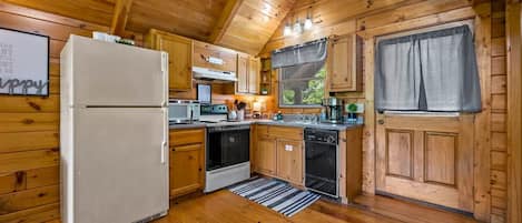 A wooden cabin kitchen with a refrigerator, oven, dishwasher, and wooden cabinets.