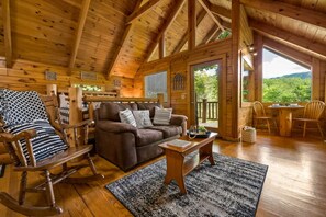 A cozy cabin interior with a brown leather sofa, wooden rocking chair, and a dining table with chairs. - Private Studio Log Cabin  Hot Tub Fireplace Relax (Sevierville)