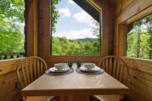 A wooden dining table with two chairs, set for two, and a view of a forest through a large window. - Private Studio Log Cabin  Hot Tub Fireplace Relax (Sevierville)