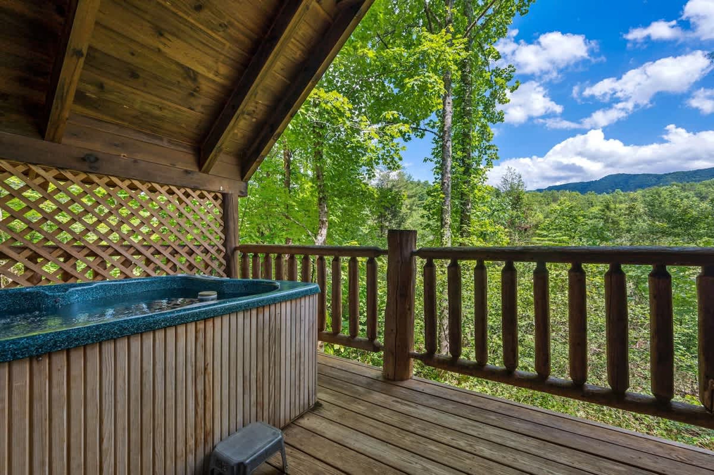 A wooden deck with a hot tub, wooden railings, and a view of a forested area.