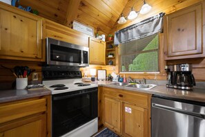 A wooden cabin kitchen with a stove, microwave, sink, and coffee maker. - Private Studio Log Cabin  Hot Tub Fireplace Chill (Sevierville)