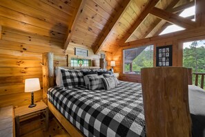 A wooden cabin bedroom with a checkered bedspread, a nightstand with a lamp, and a window with blinds. - Private Studio Log Cabin  Hot Tub Fireplace Chill (Sevierville)
