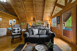 A cozy cabin interior with a wooden ceiling, a black sofa with patterned cushions, a wooden rocking chair, and a dining table. - Private Studio Log Cabin  Hot Tub Fireplace Chill (Sevierville)