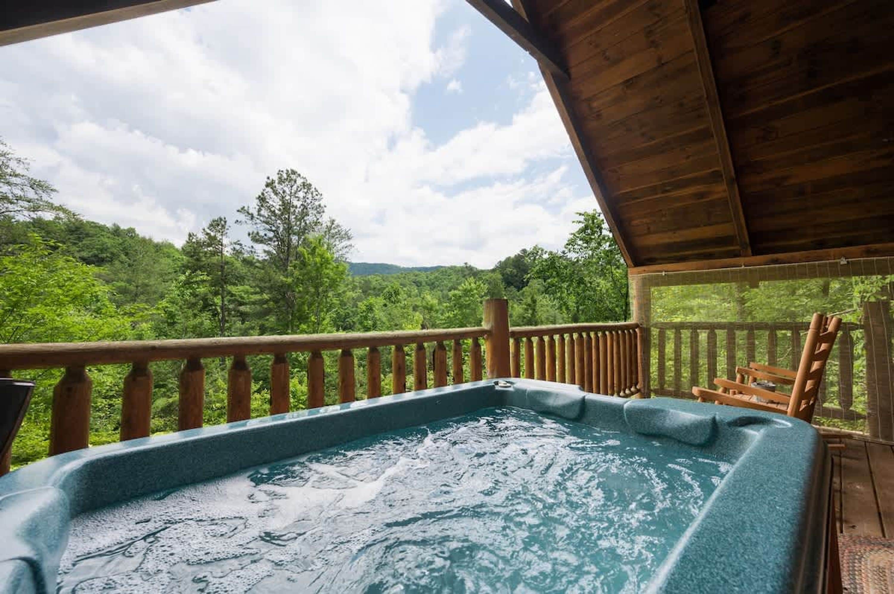 A hot tub on a wooden deck with a view of a forested landscape.