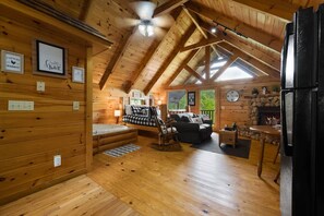 Ein gemütliches Blockhaus-Interieur mit Schlafzimmer im Zwischengeschoss, Kamin, Holzwänden und Essbereich.