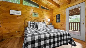 Acogedor dormitorio de cabaña de madera con colcha de cuadros, una mesita de noche con lámpara, y un letrero que dice 'cada momento cuenta'.