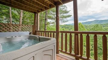 Un jacuzzi en una terraza de madera con vistas a una cadena montañosa boscosa.