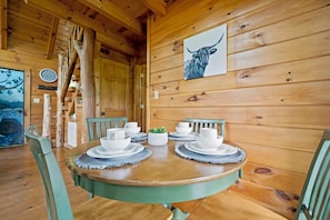 Una mesa de comedor de madera dispuesta con platos, tazones y tazas blancos, rodeada de sillas verdes.
