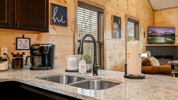 A kitchen with a granite countertop, a coffee maker, a kettle, and a sink.