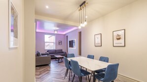 Un espace repas moderne avec une table blanche et des chaises bleues, un canapé et un luminaire suspendu au plafond.