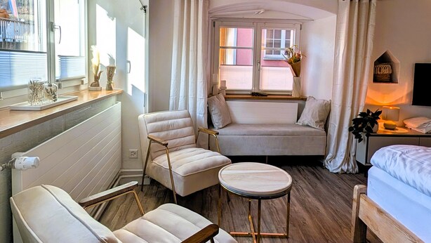 A cozy room with a wooden ceiling, a sofa, two armchairs, a small round table, and a bed.