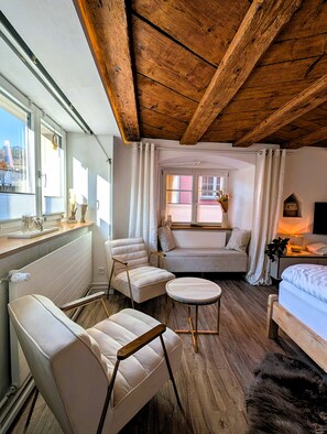Une pièce chaleureuse avec un plafond en bois, un canapé, deux fauteuils, une petite table ronde et un lit.