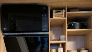 A compact kitchen with a microwave, a stove, a sink, and wooden shelves above holding kitchenware.
