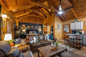A cozy cabin interior with a wooden ceiling, a fireplace, a dining area, and a kitchen. - Location-Quiet-HotTub-Fireplace (Pigeon Forge)