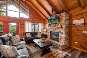 A cozy cabin interior with a stone fireplace, wooden walls, and a leather sofa. - View-Location-Hot Tub-Pool Table-3 Fireplaces (Sevierville)