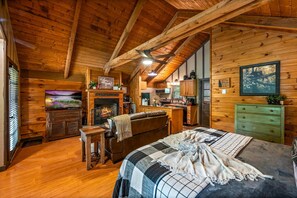 Ein Schlafzimmer in einer Blockhütte mit Kamin, einem Bett, einem Schreibtisch und einer Küchenzeile.