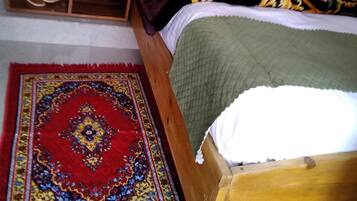 A bedroom with a wooden bed, a nightstand with a kettle, cups, and a tray, and a red patterned rug.