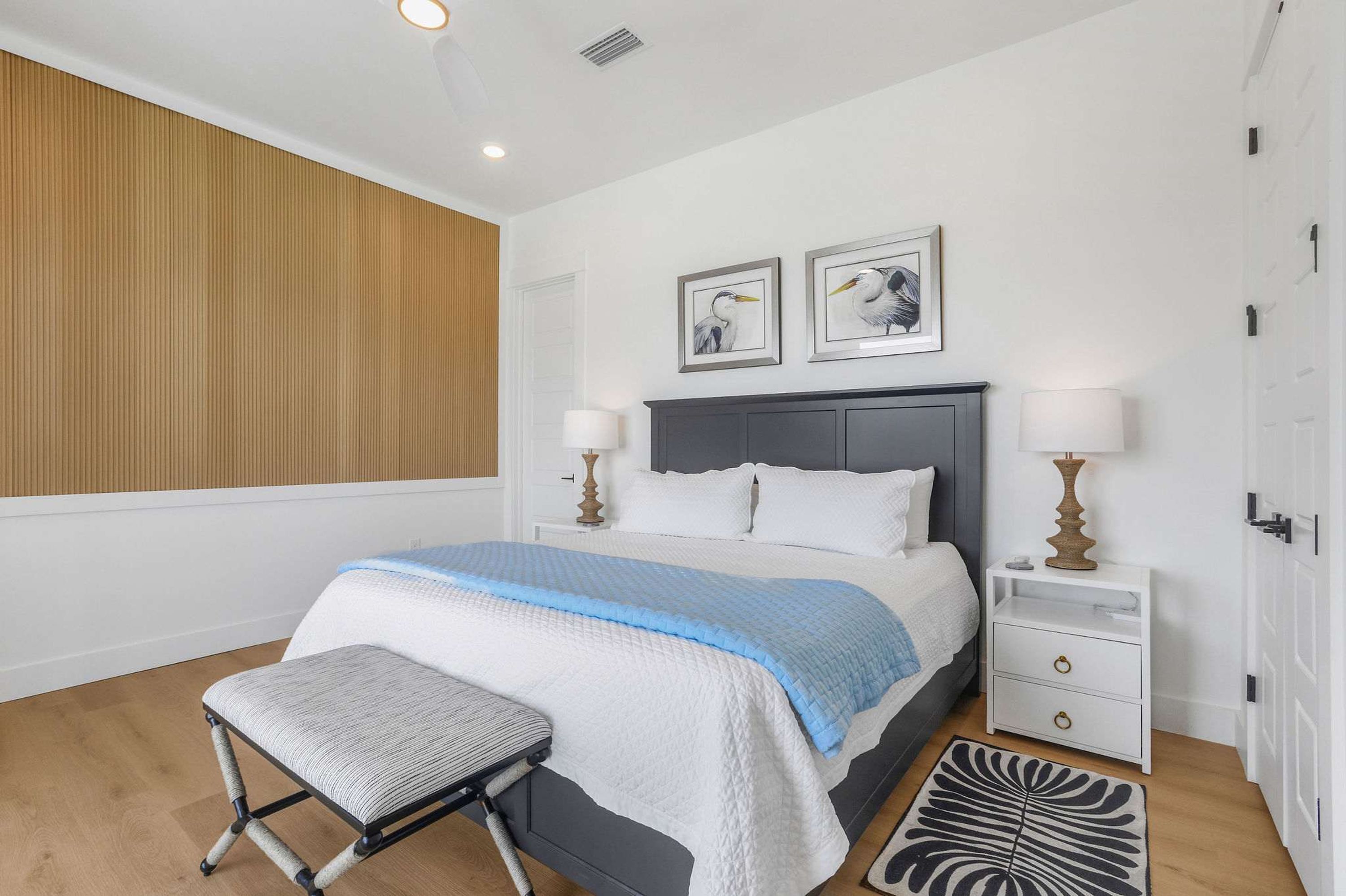 A bedroom with a bed, bedside tables, a bench, and artwork on the wall.