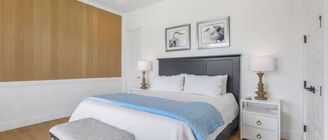 A bedroom with a bed, bedside tables, a bench, and artwork on the wall.