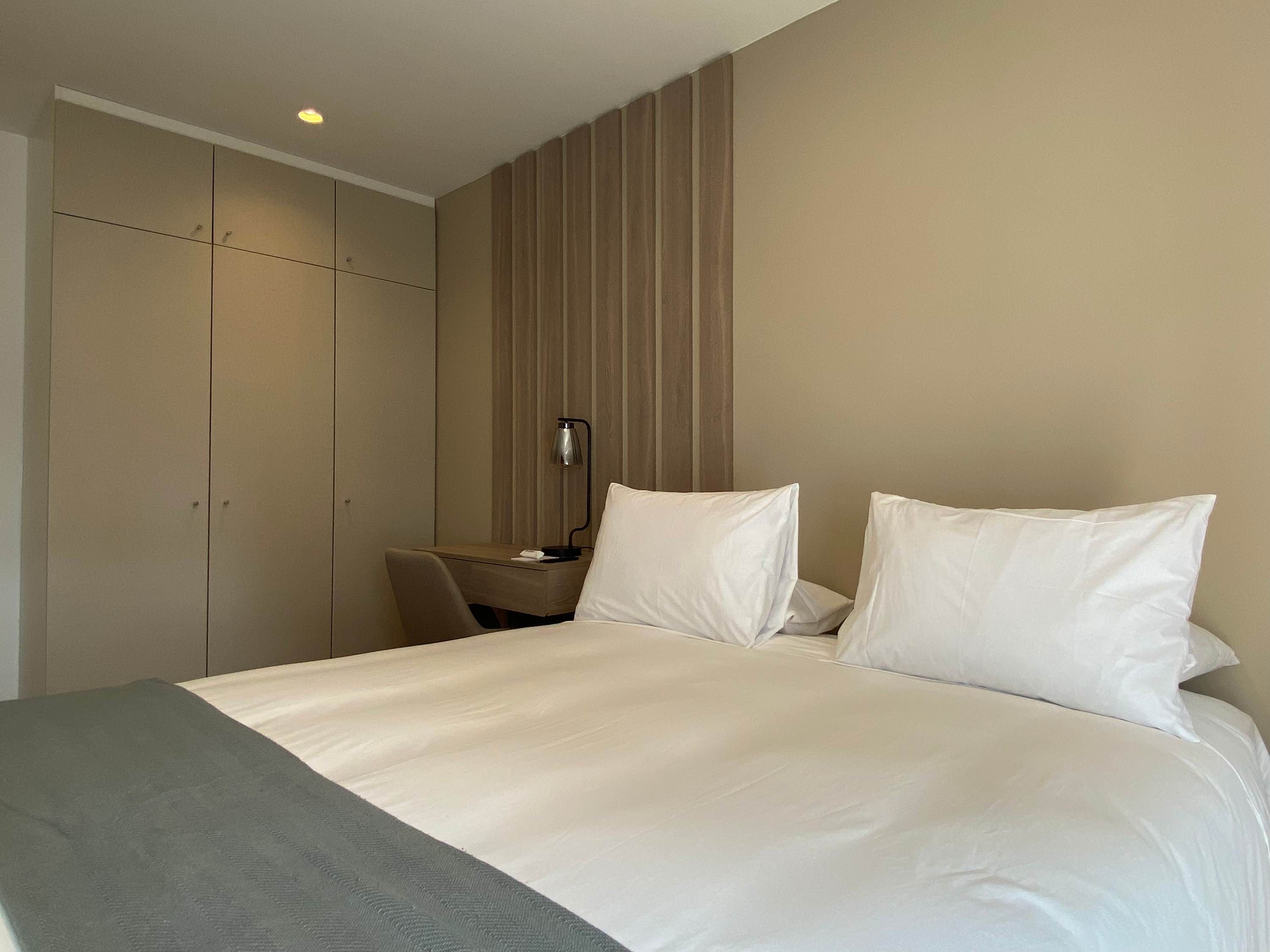 A hotel room with a large bed, a desk, and a wardrobe.